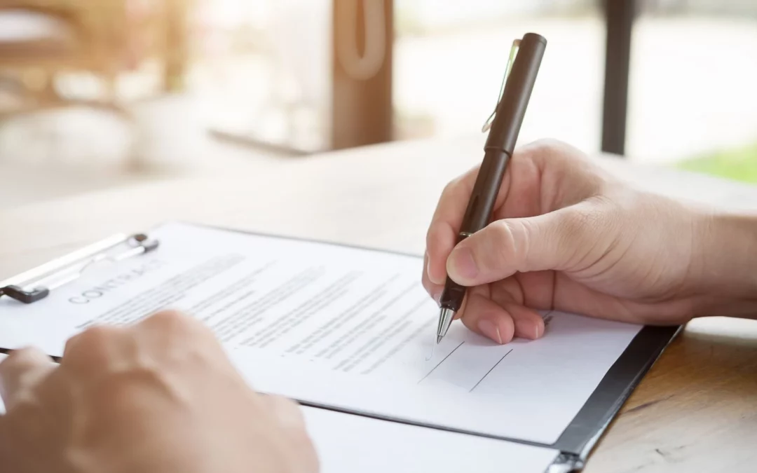 Une personne est sur le point de signer avec un stylo noir un contrat écrit qui est posé sur une table.